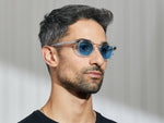 Model ma na sobie okulary The GELT w kolorze Crystal w rozmiarze 46 z soczewkami przyciemnianymi Celebrity Blue.